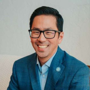 Man wearing glasses, blue suit jacket, smiling at the camera.