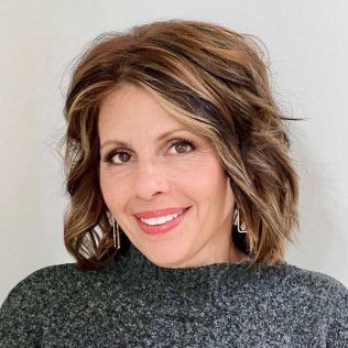 Woman with brown hair and highlights, smiling, wearing a gray sweater.