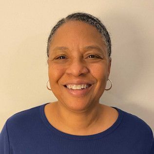 Woman with short, graying hair smiles, wearing a blue shirt and hoop earrings.