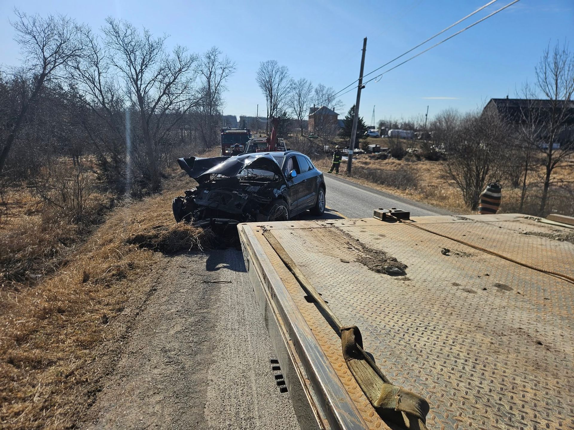 A severely damaged car is loaded onto a tow truck on a rural road, sunny day.
