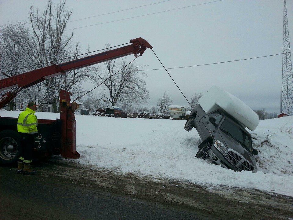 Tow truck pulling a vehicle out of a snow-covered ditch on a cloudy day.