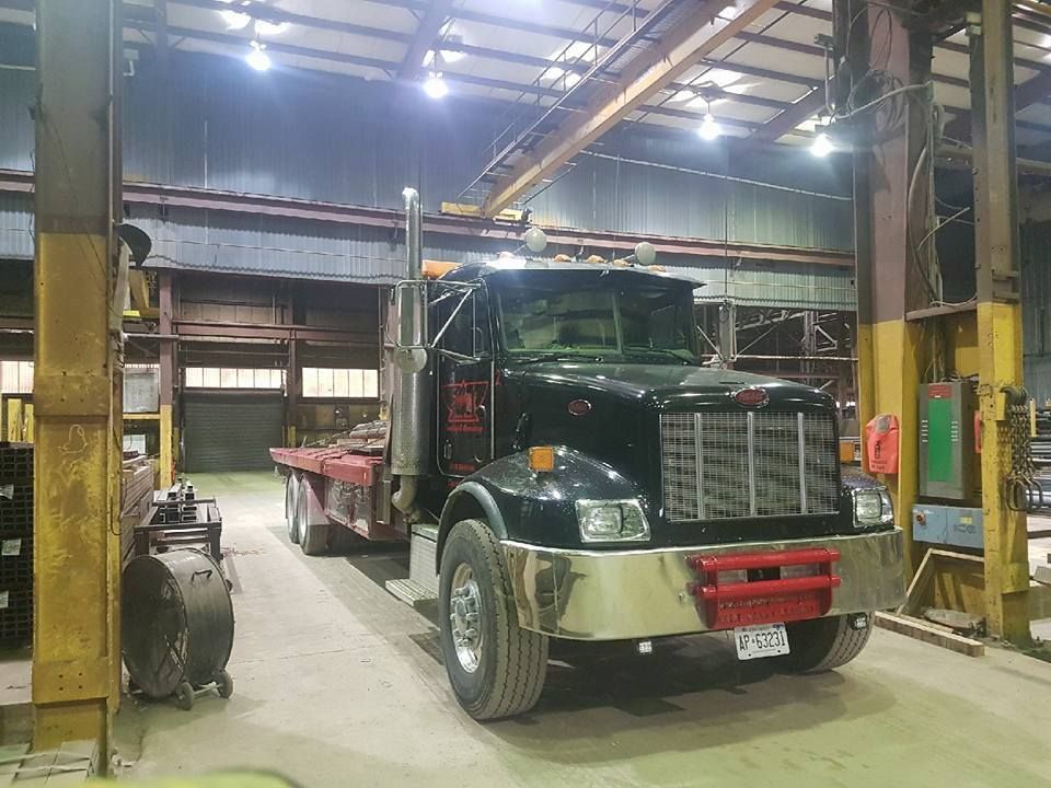 Black truck with flatbed trailer inside a warehouse, under bright lights.