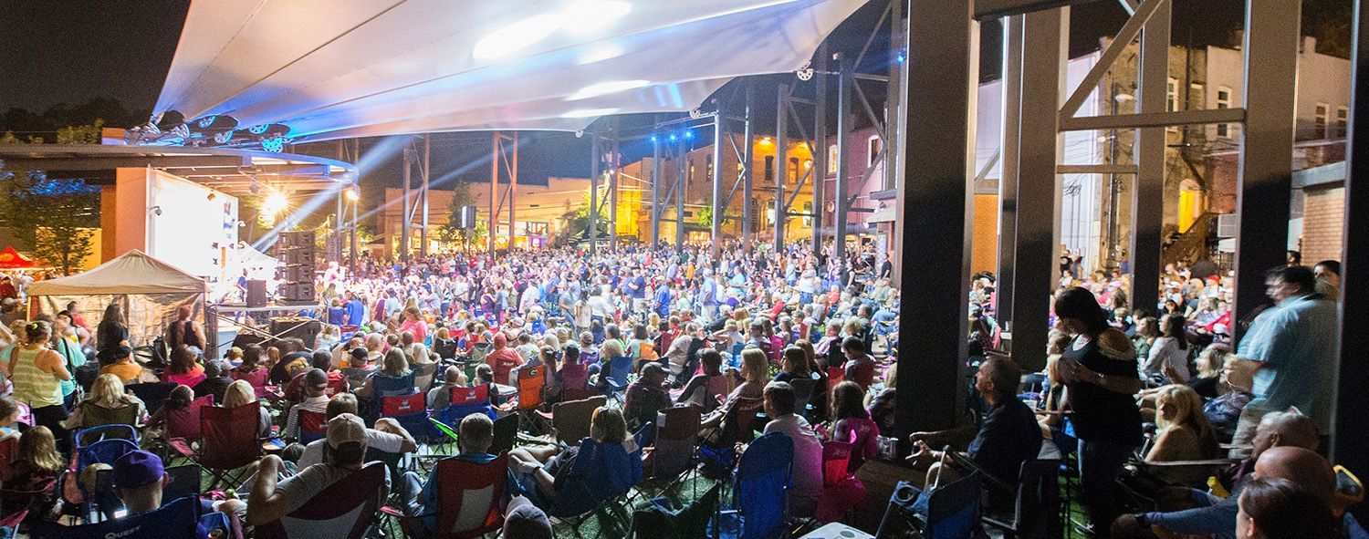 A large crowd of people are sitting under a tent at a concert.
