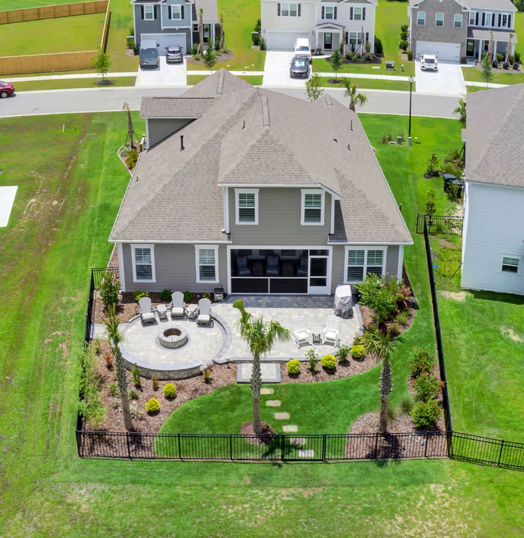Aerial view of a gray two-story house with a backyard patio, fire pit, and palm trees surrounded by green grass.