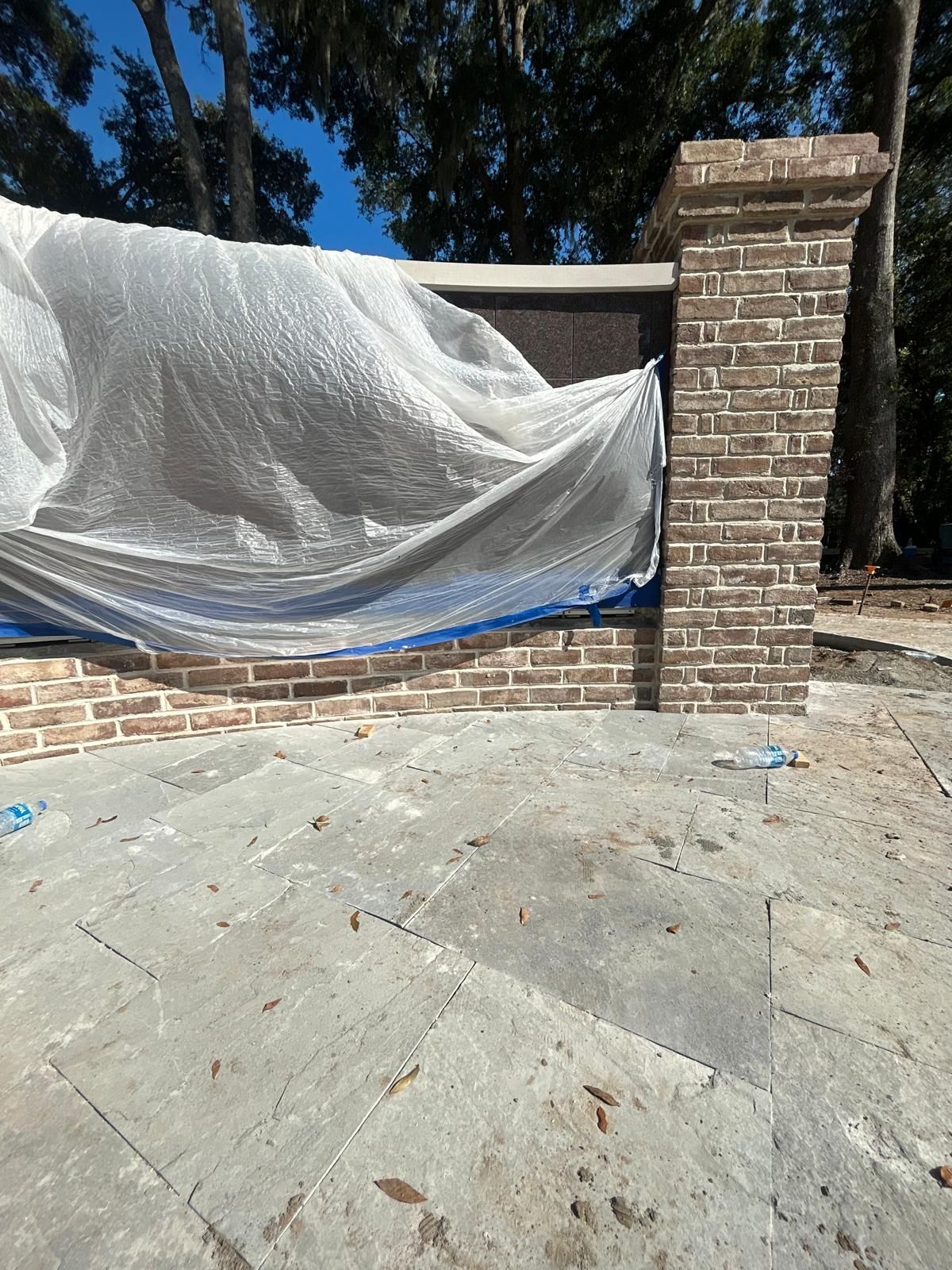 Brick wall and pillar covered with a tarp, on a concrete surface, sunny outdoor setting.
