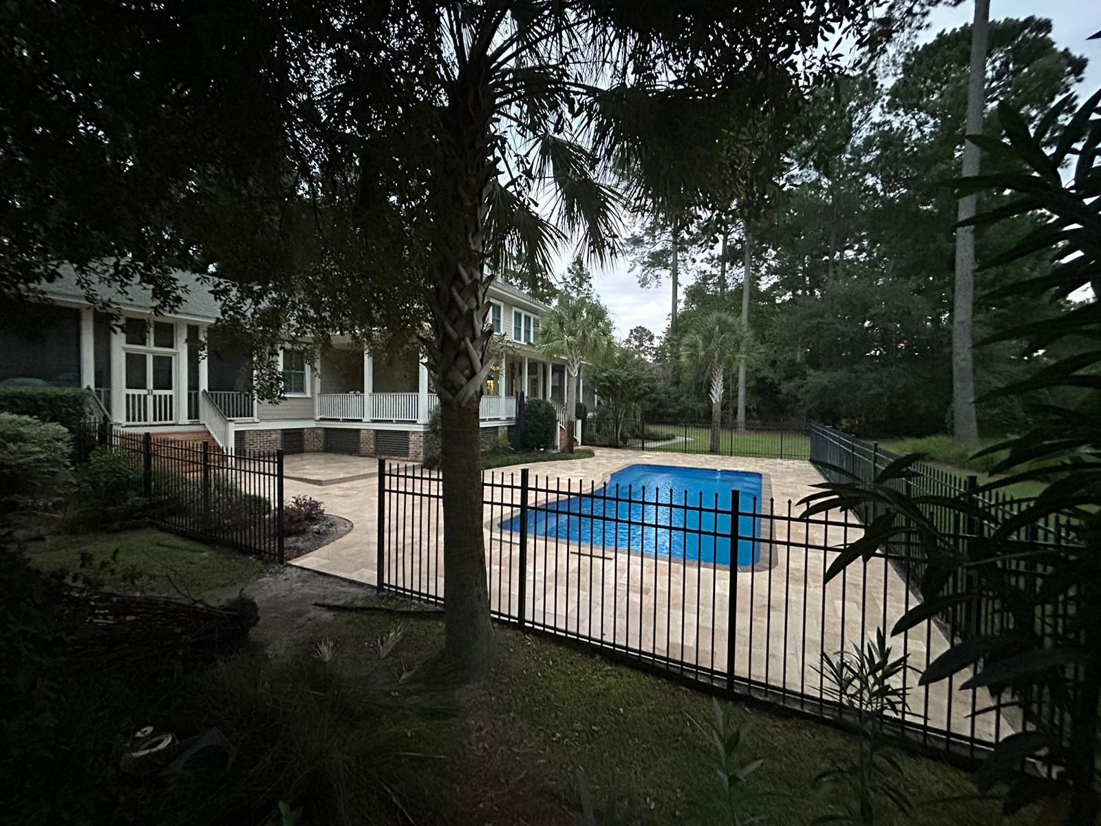 A fenced-in pool with a blue cover, next to a house with a porch, in a wooded area.
