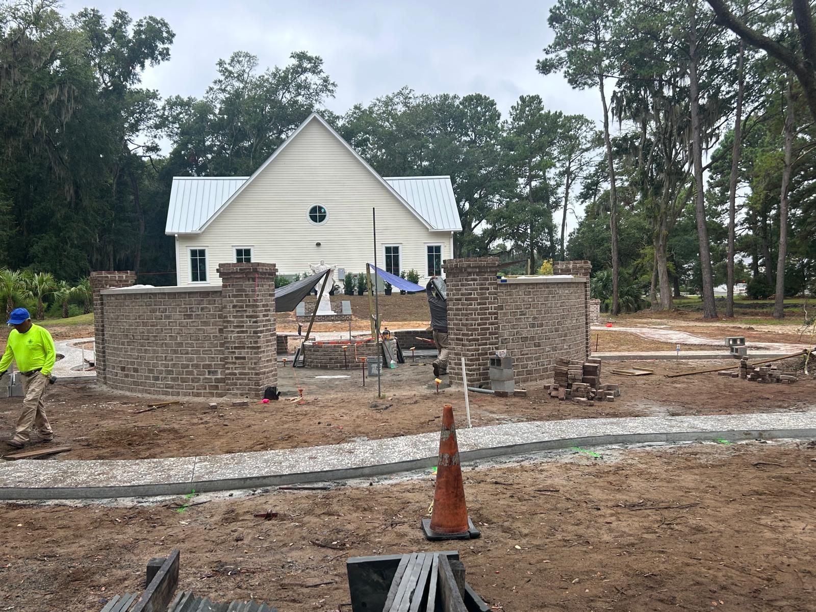Construction site: brick walls being built in front of a white church. A worker in a neon green shirt is present.