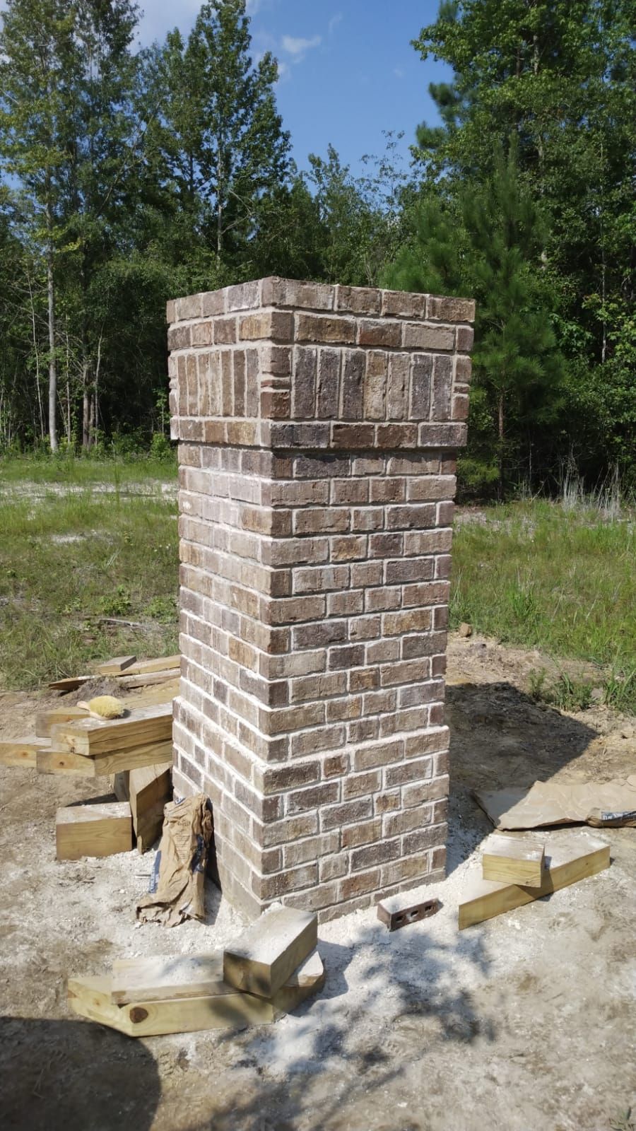 Brick chimney under construction, brown bricks, surrounded by debris, outdoors.