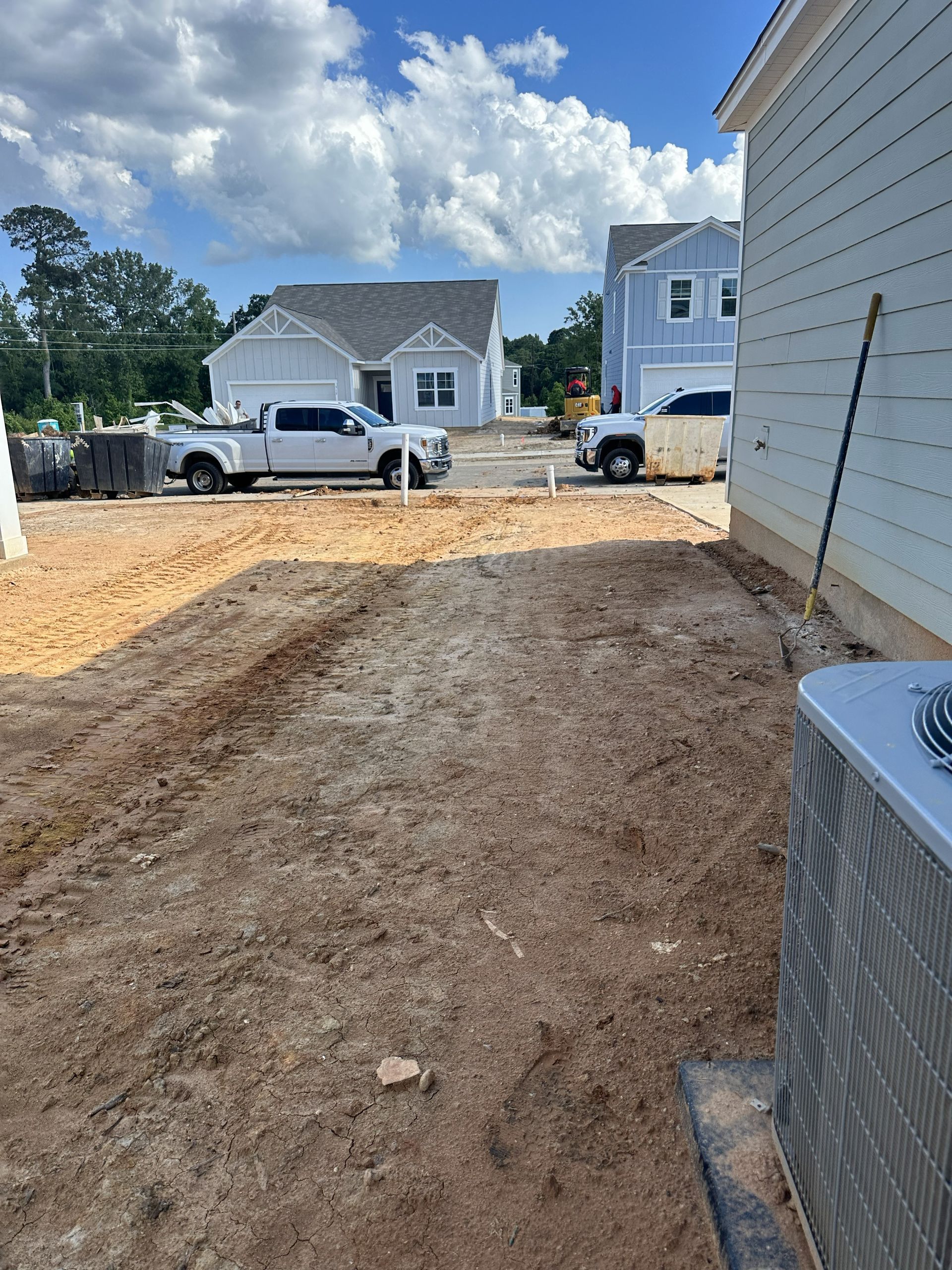 Construction site with two white pickup trucks. New homes under construction, brown dirt, and blue sky.