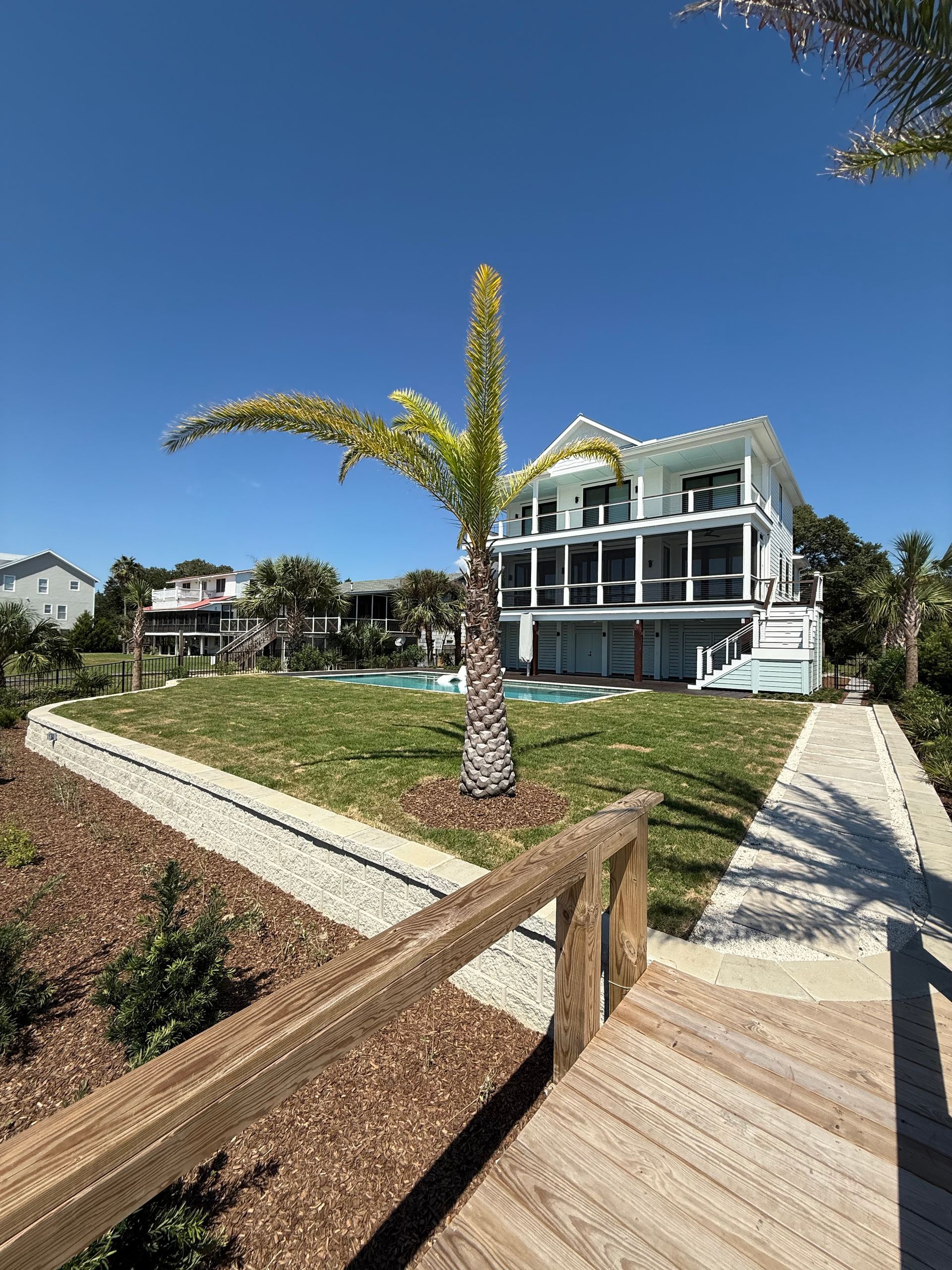 Beachfront house with a palm tree, blue sky, and a boardwalk leading toward it.