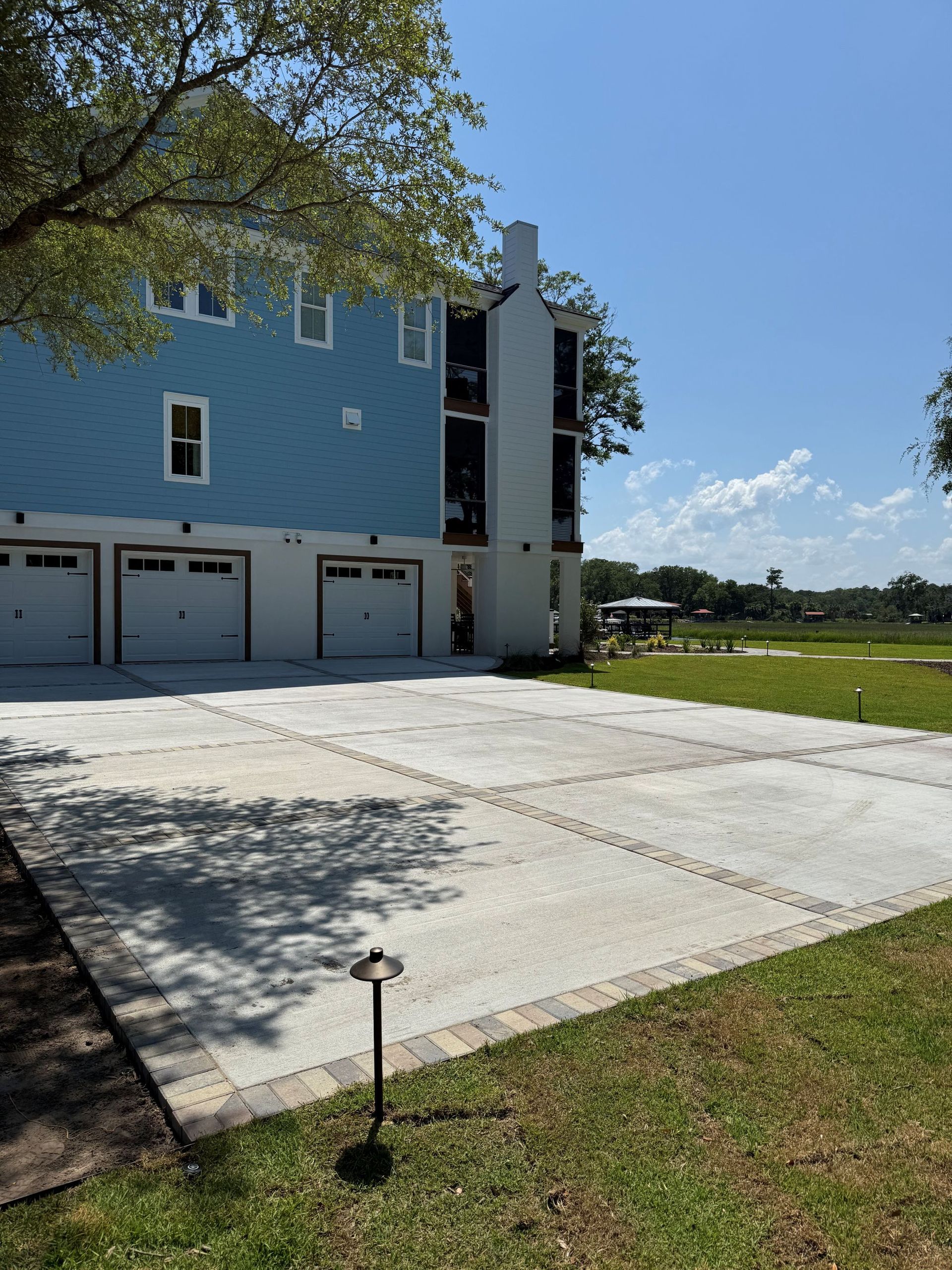 Blue house with white garage doors and concrete driveway bordering green grass, sunny day.