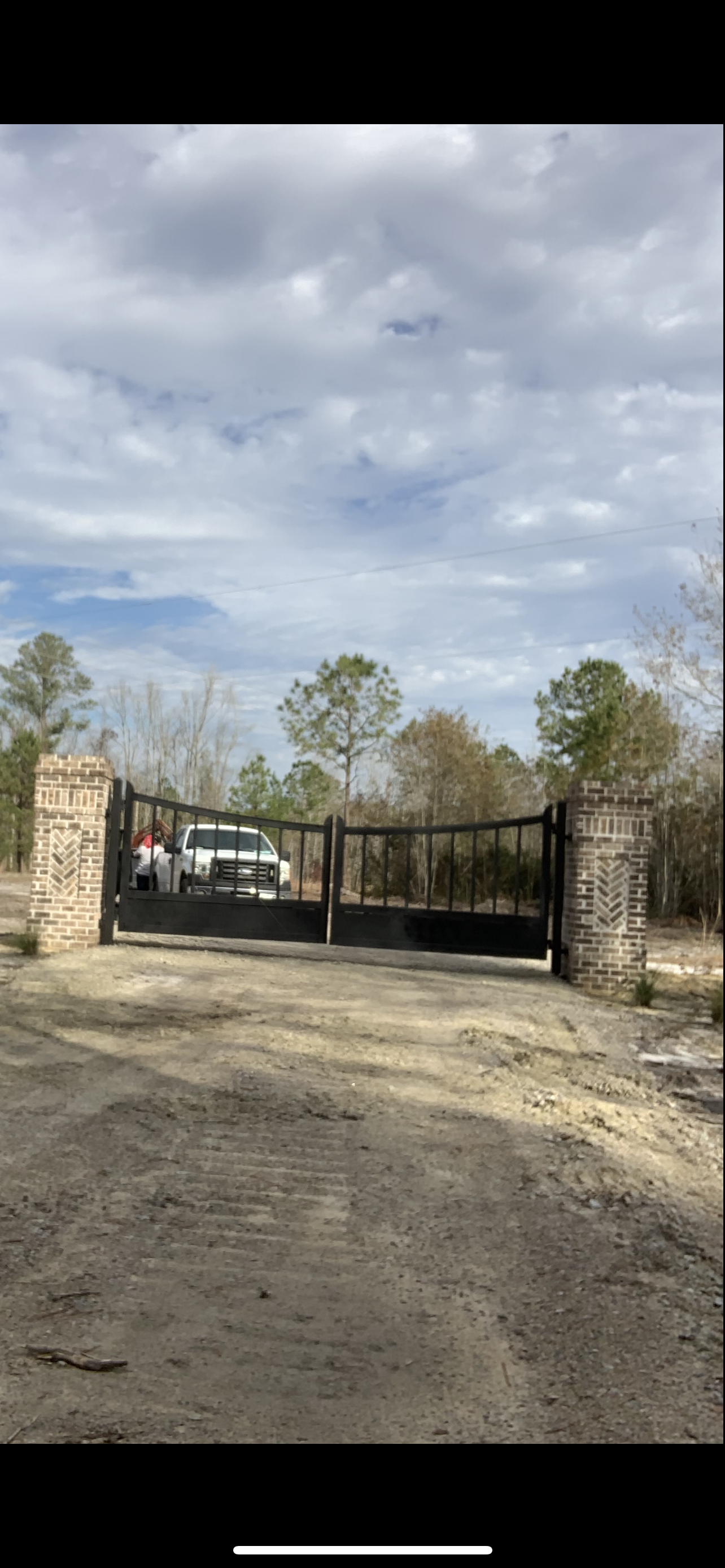 A gated entrance to a property with a vehicle parked inside. Cloudy sky overhead.