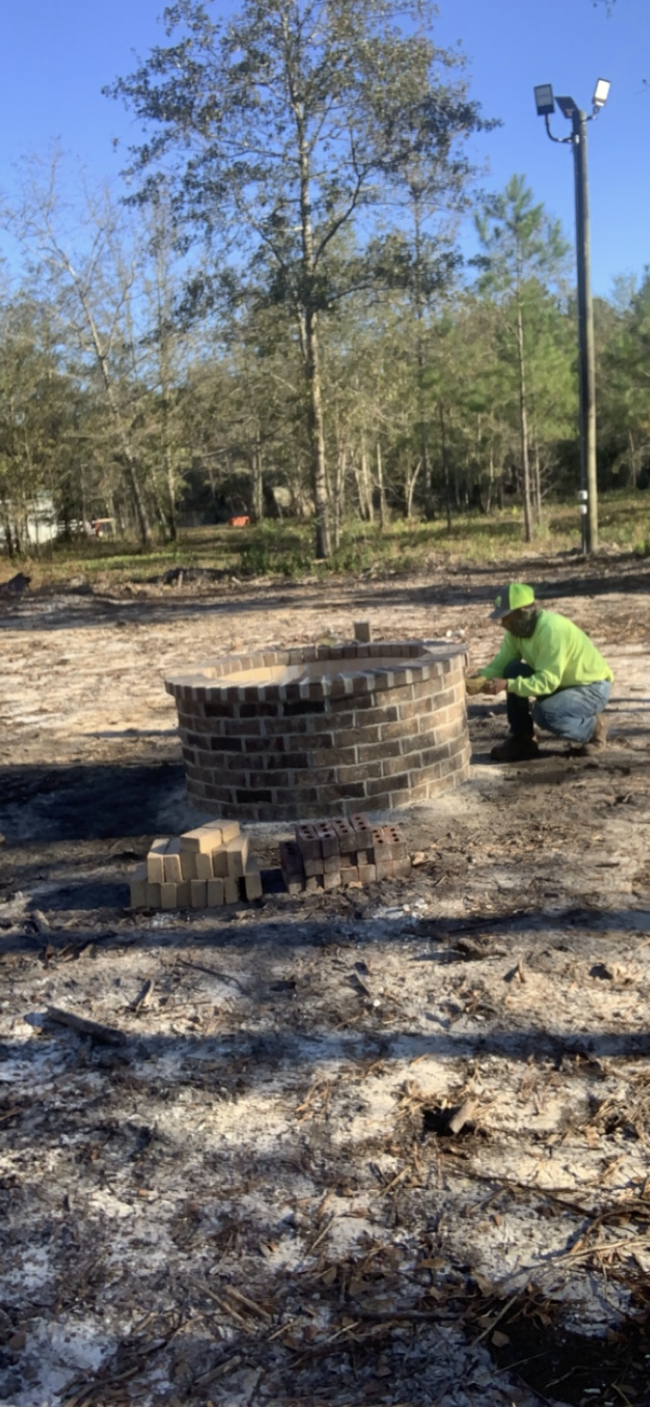 A person in a lime-green shirt working on a brick circular structure in a dirt field.