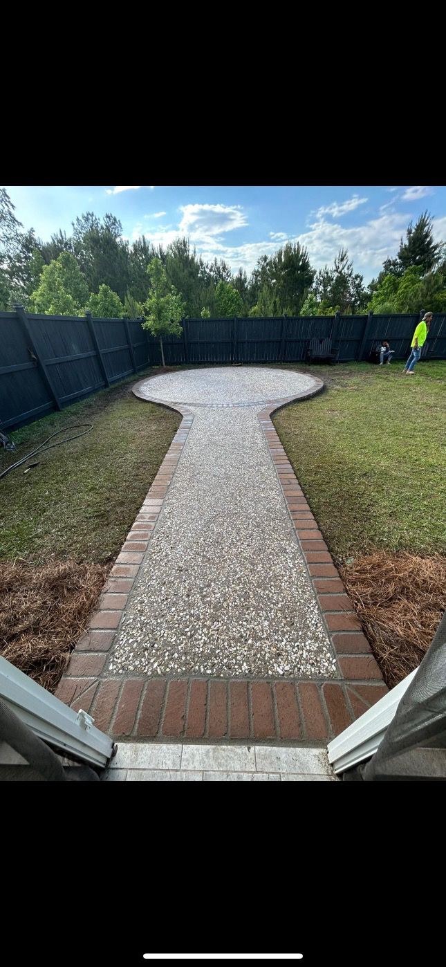 Pathway of pebbles and bricks through a grassy yard leading to a wider circular area, against a black fence.
