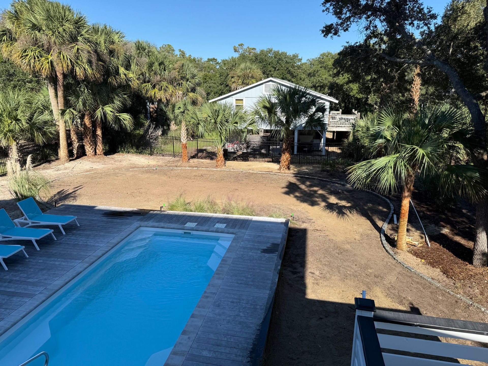 Pool and house in a tropical setting with palm trees and sun.
