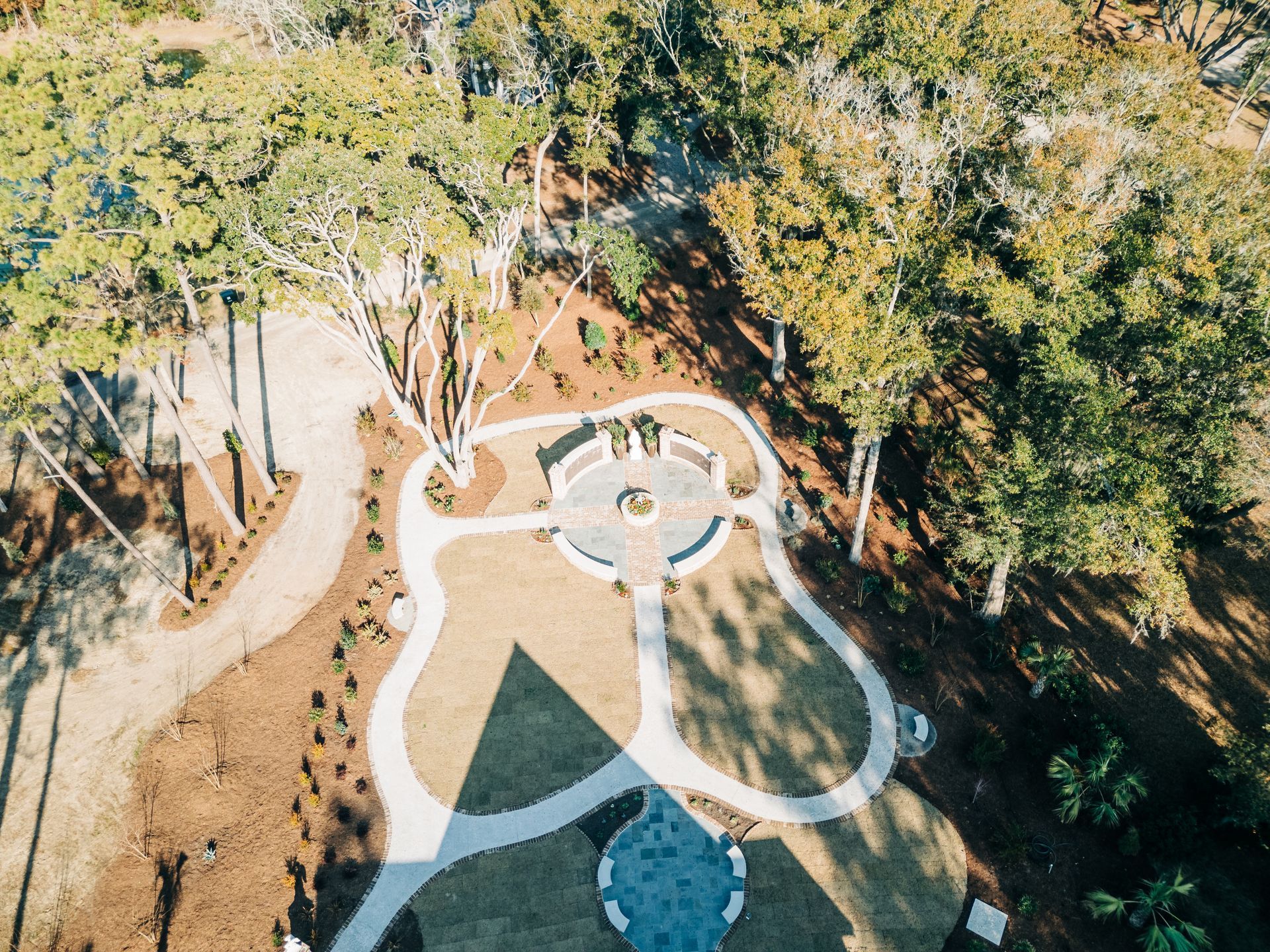 Aerial view of a paved outdoor area with paths, a central circular structure, trees, and brown mulch.