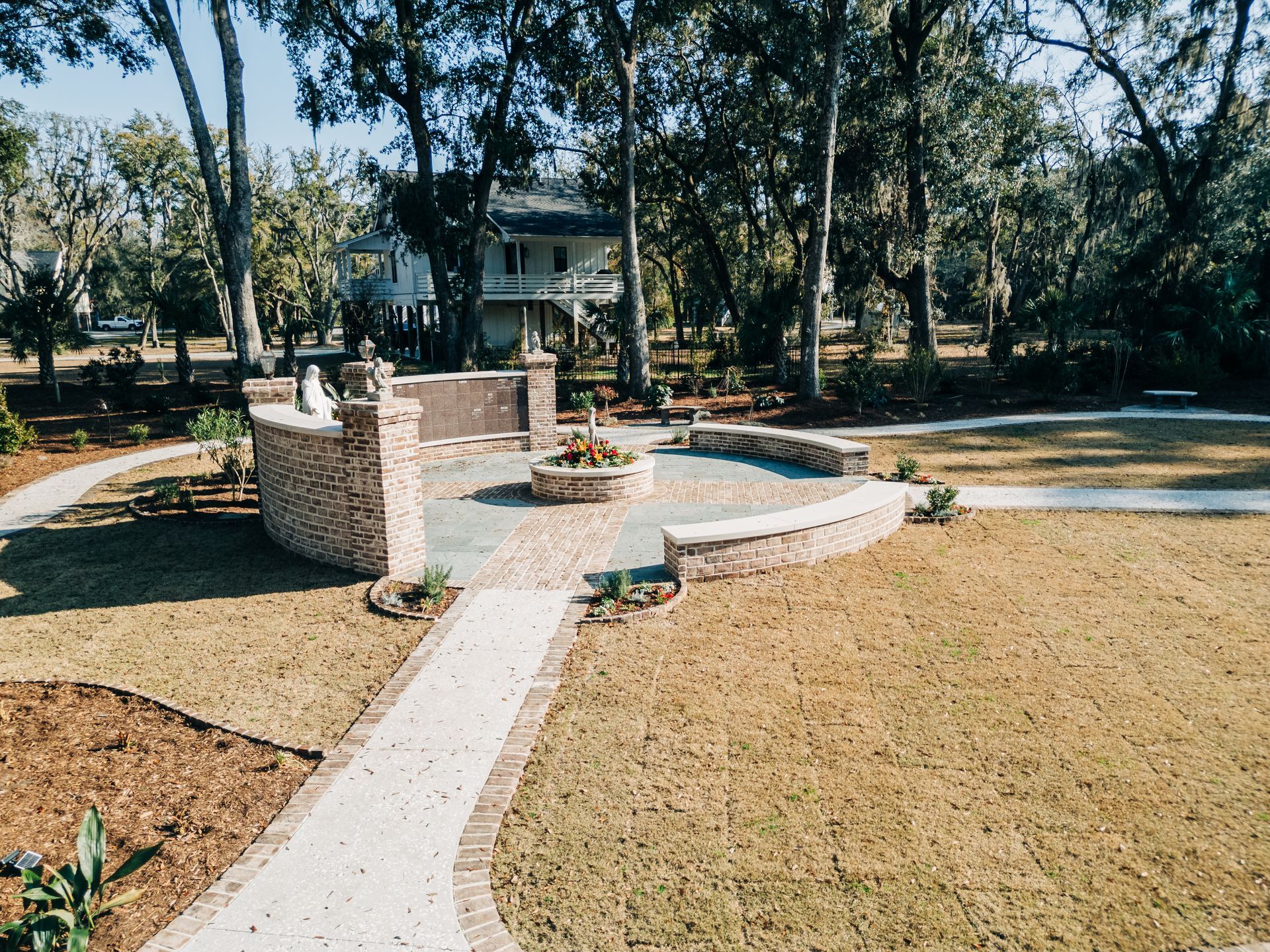 Stone patio and brick walkways in a grassy yard, surrounded by trees; a two-story house is in the background.