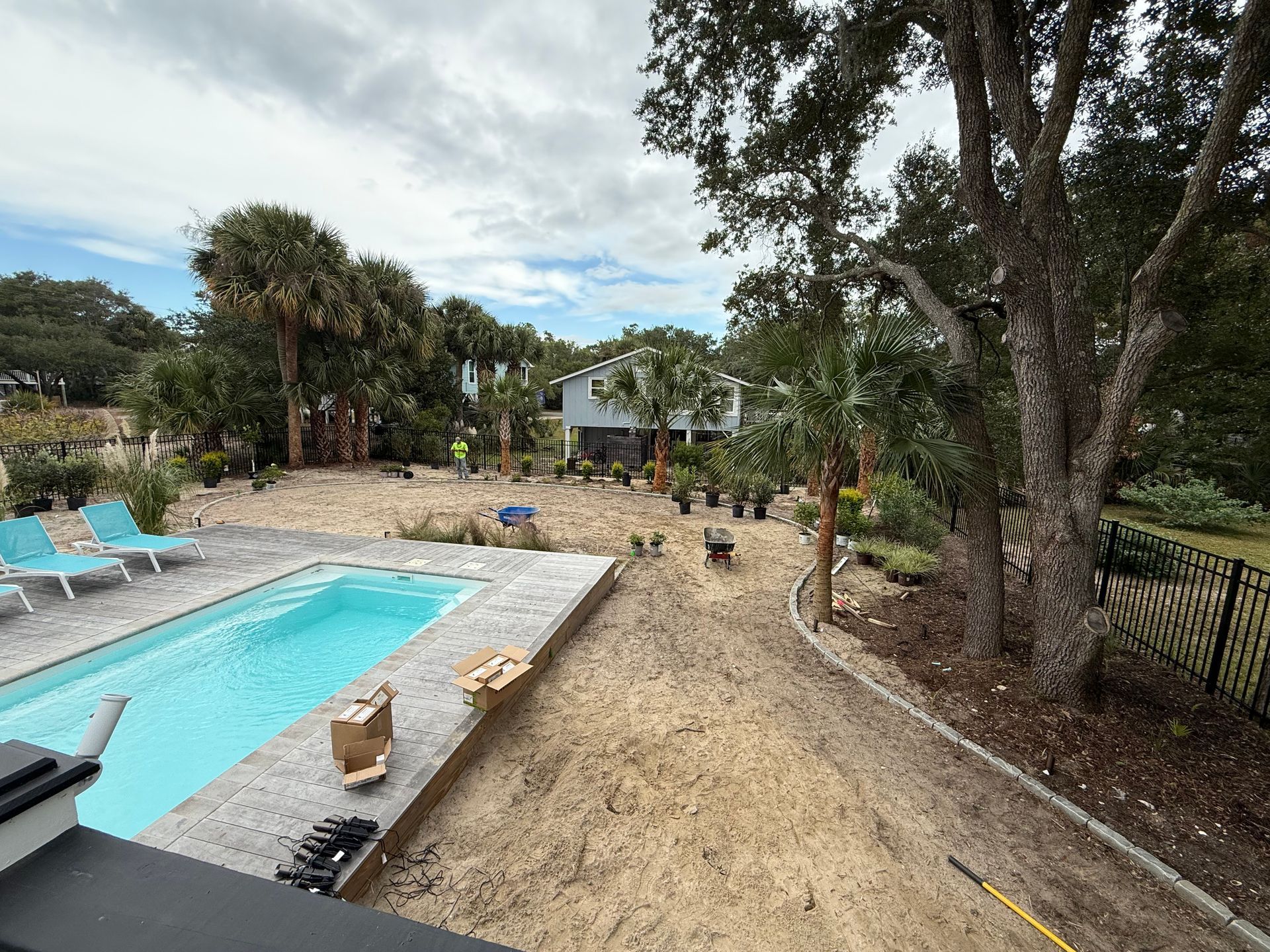Poolside construction with a pool, sand, and potted plants under a cloudy sky.