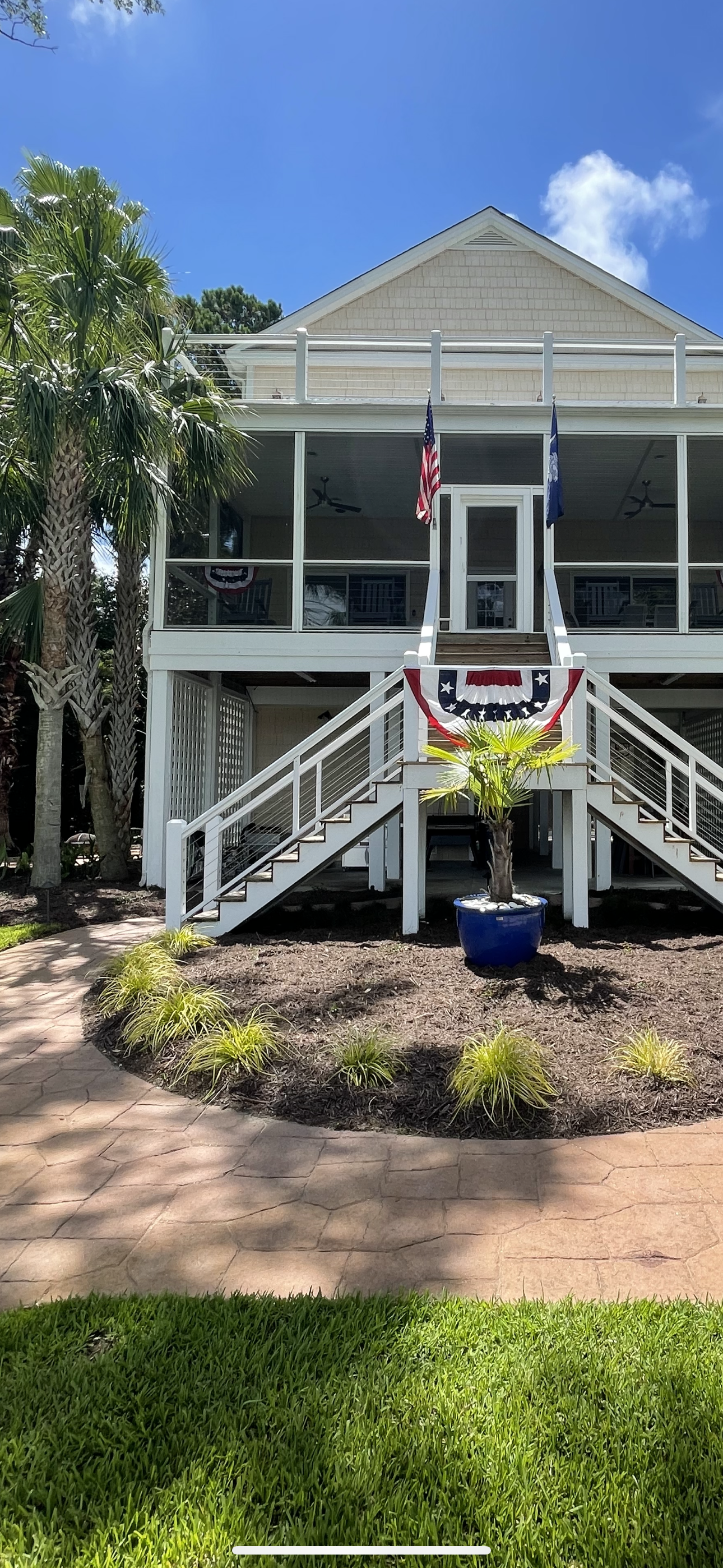 White house with a screened porch and American flag, stairs leading to the entrance, blue sky.