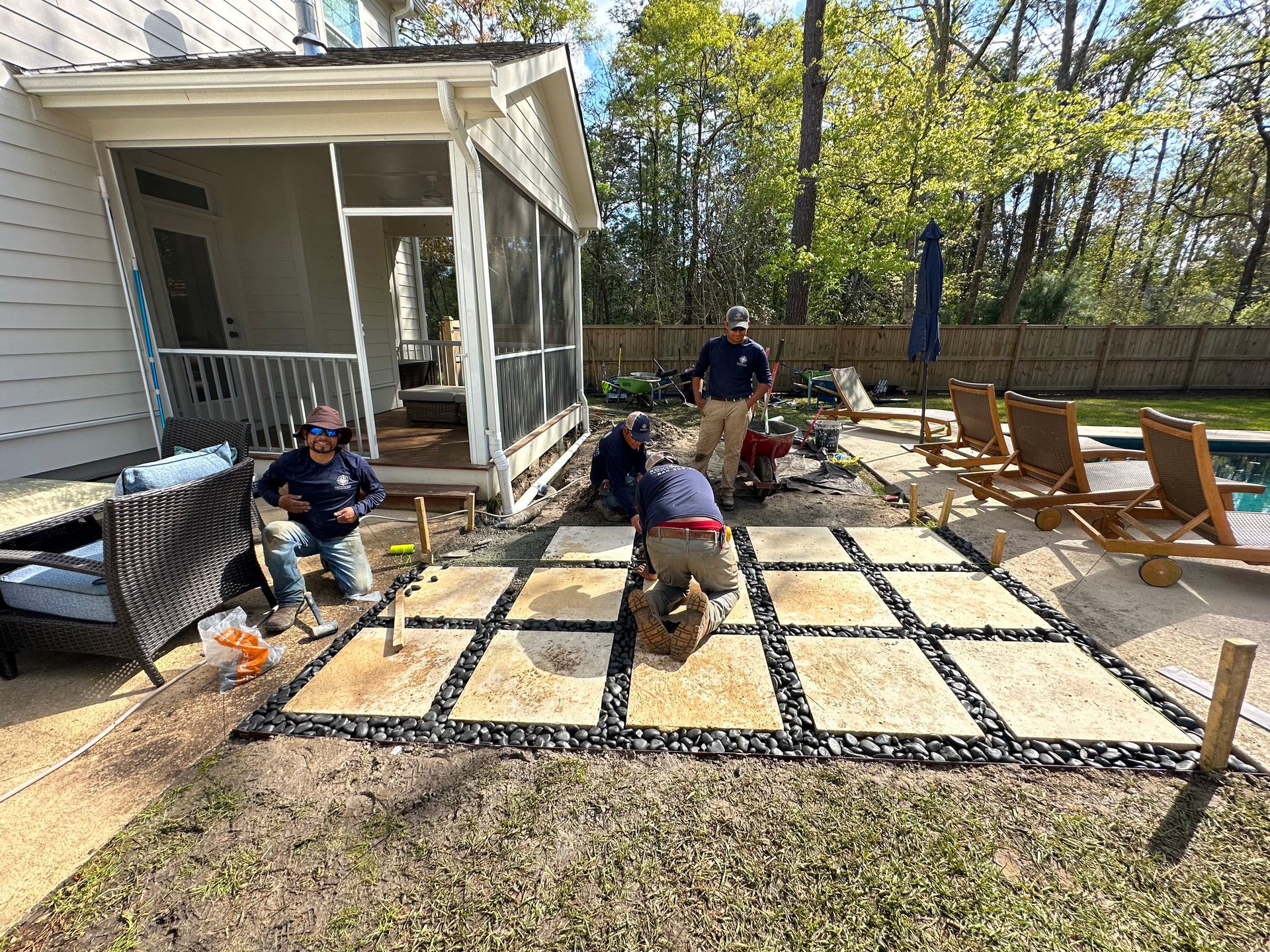Construction workers installing stone pavers next to a pool.