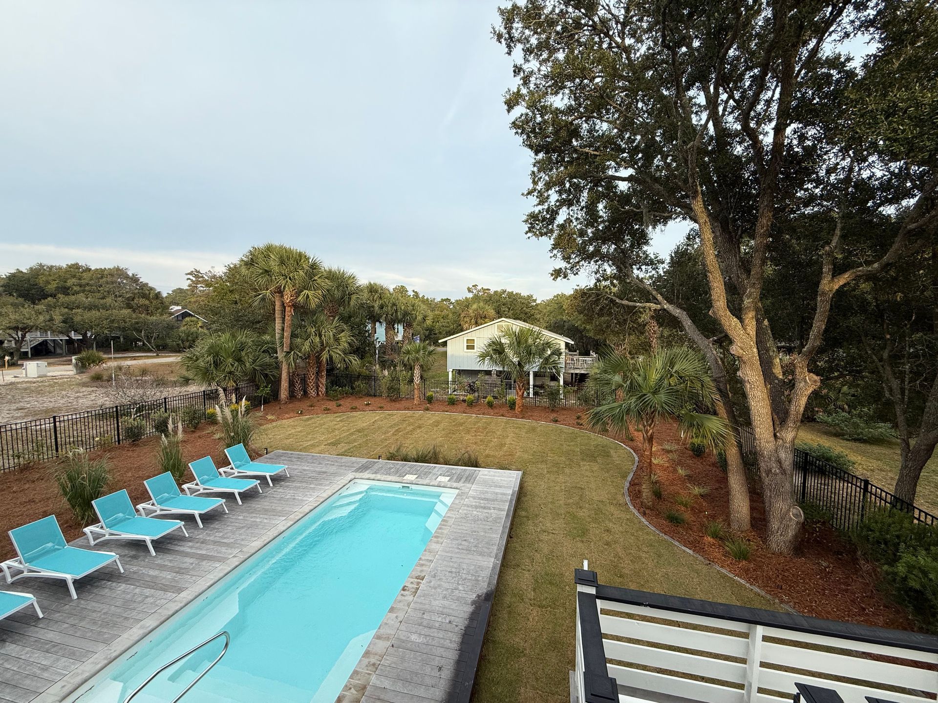 Outdoor pool with turquoise water and lounge chairs, surrounded by landscaping, trees and a house.
