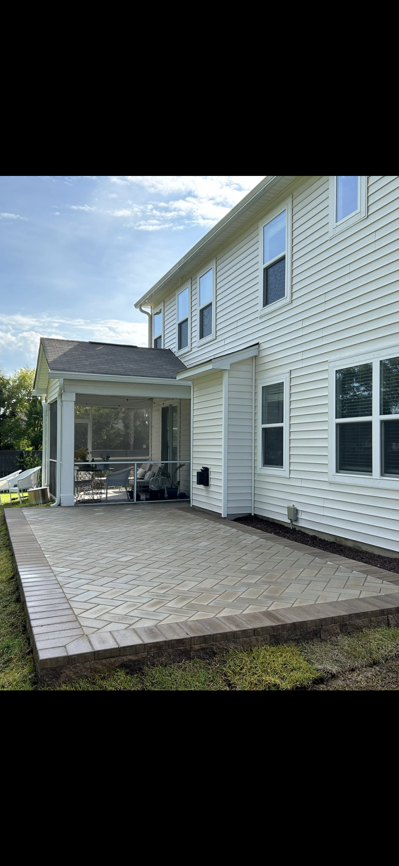 Backyard patio with paved area, screened porch, and white siding house.