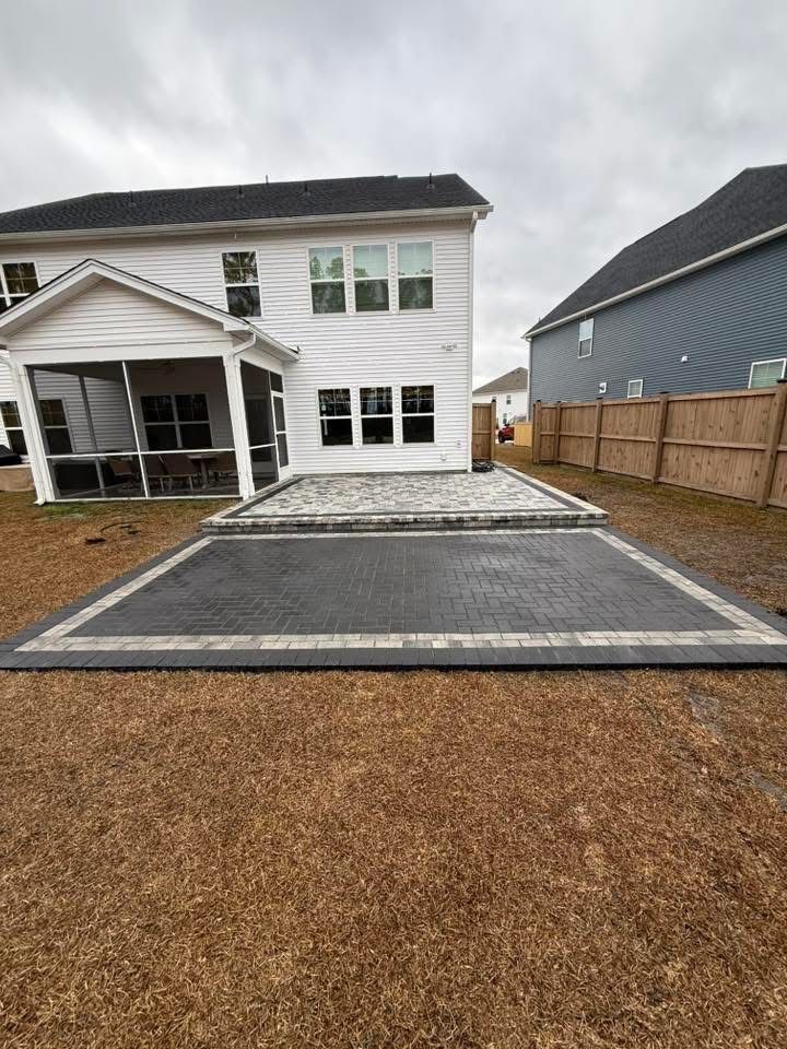Backyard patio with brick pavers. A white house and a neighboring blue house are visible. Overcast day.
