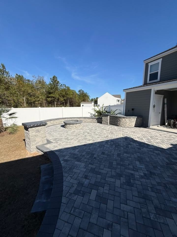 Outdoor patio with gray pavers and retaining walls, a fire pit, and a house.