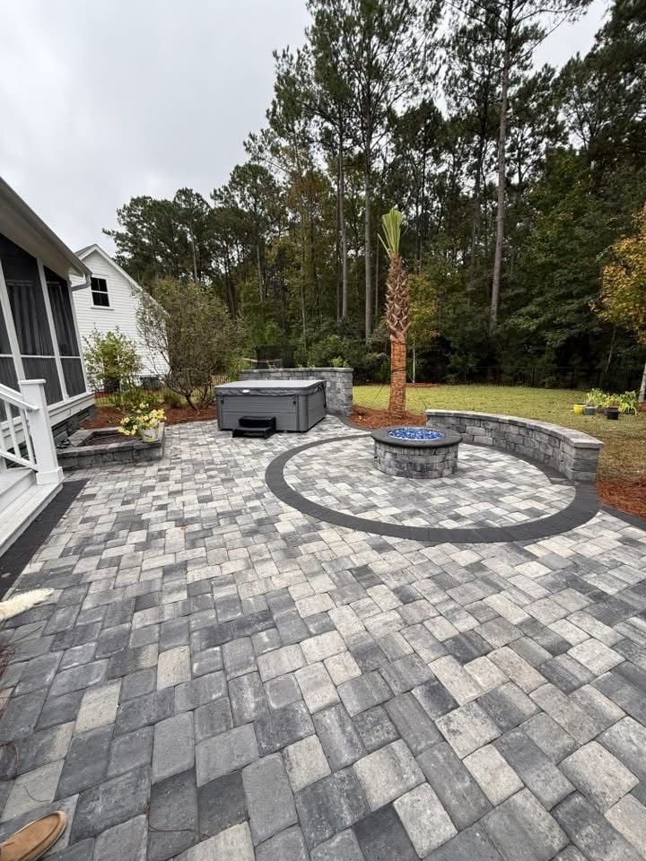 Brick patio with hot tub, fire pit, and stone walls; surrounded by trees and grass.