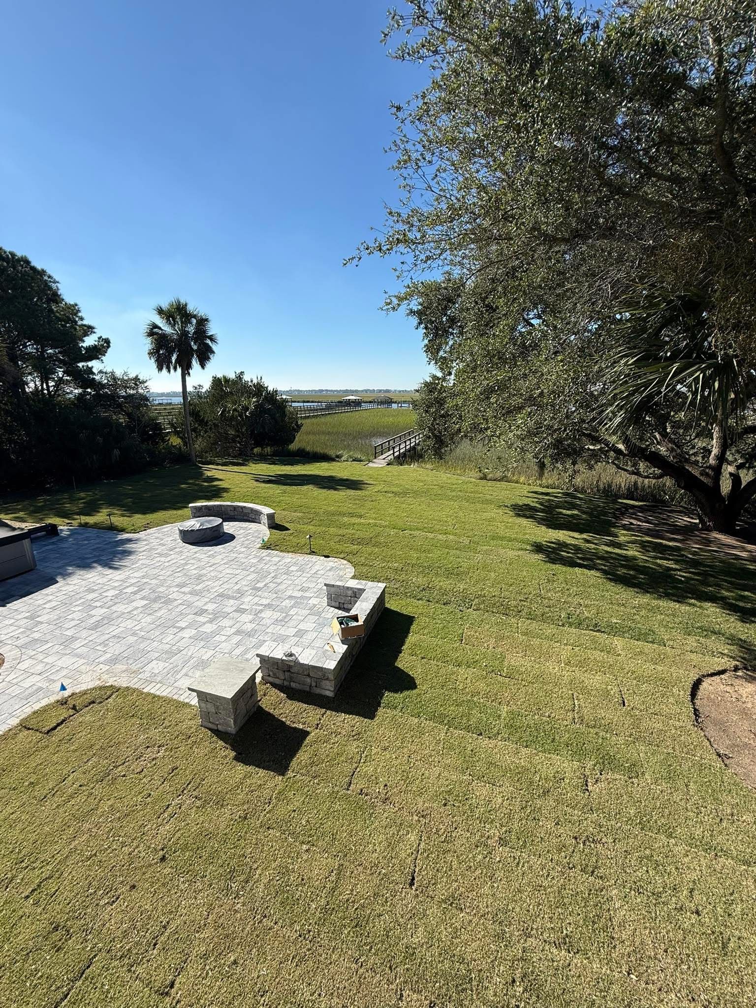 A yard with a gravel patio under construction and grass; a view of the water and sky.