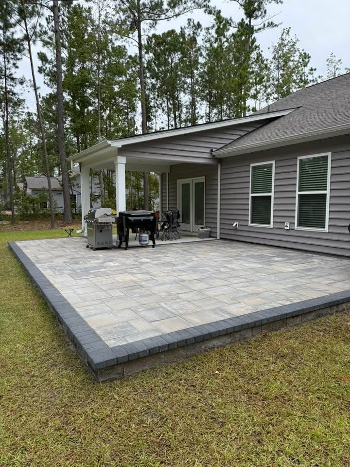 Backyard patio with gray pavers and border, leading to a covered porch with a grill.