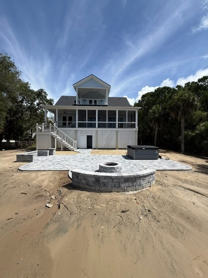 White coastal home with a screened porch, on sandy ground, with a fire pit and hot tub.
