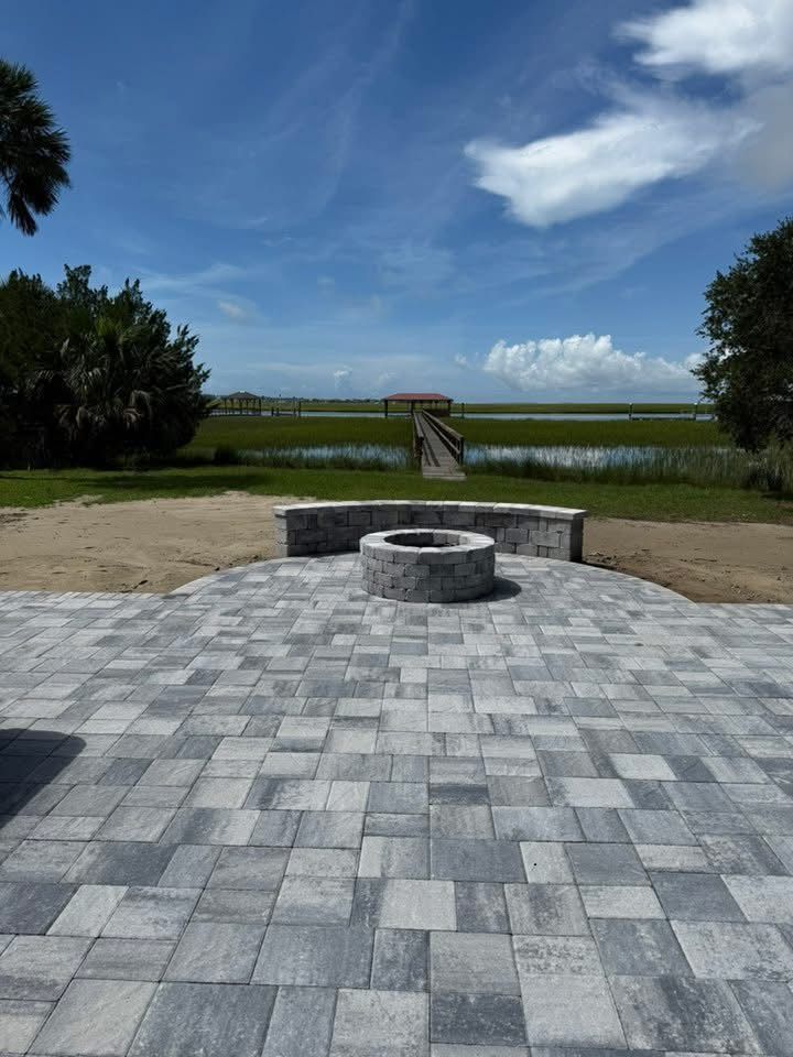Brick patio with fire pit overlooking a marsh and a dock under a blue sky.