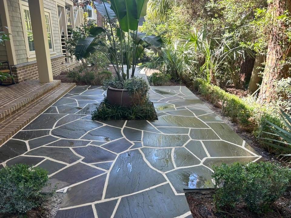 Flagstone patio with a large potted plant in the center, surrounded by greenery.