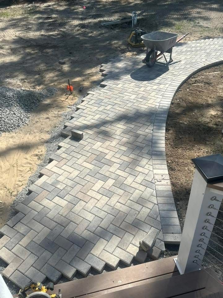 Pathway under construction: gray brick pavers, curved design, near steps and wheelbarrow.