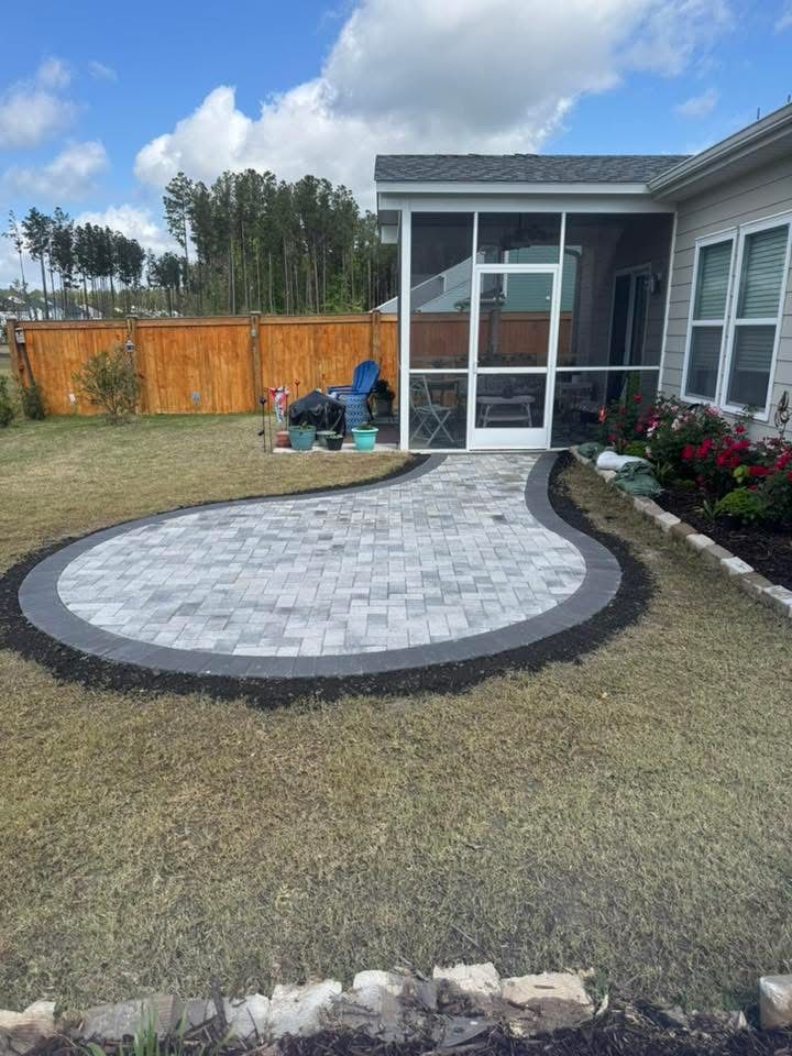 Curved paver patio with a dark border in a grassy yard, leading to a screened porch.
