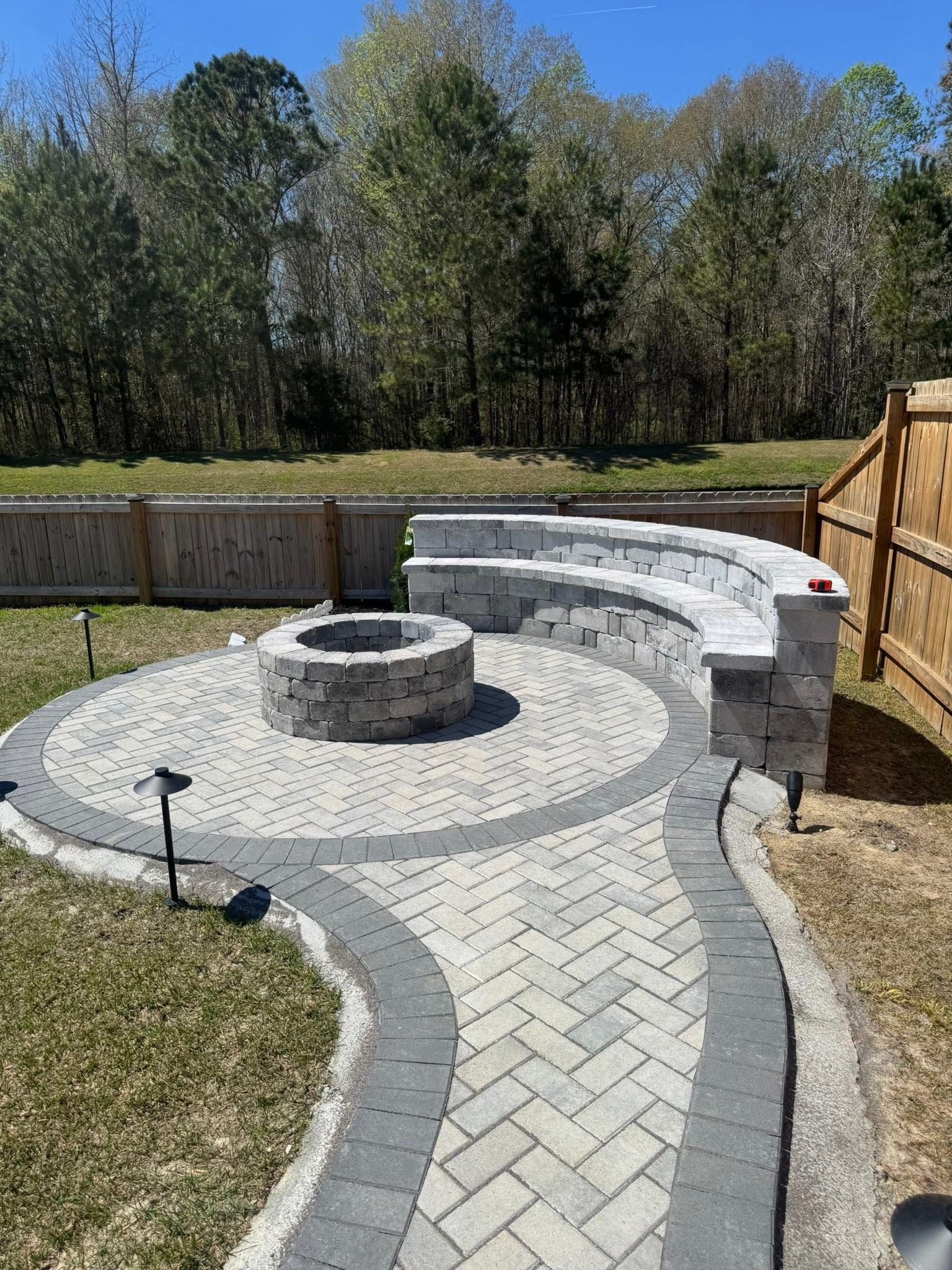 Stone patio with a fire pit and curved seating area. Pathway leads to the fire pit.