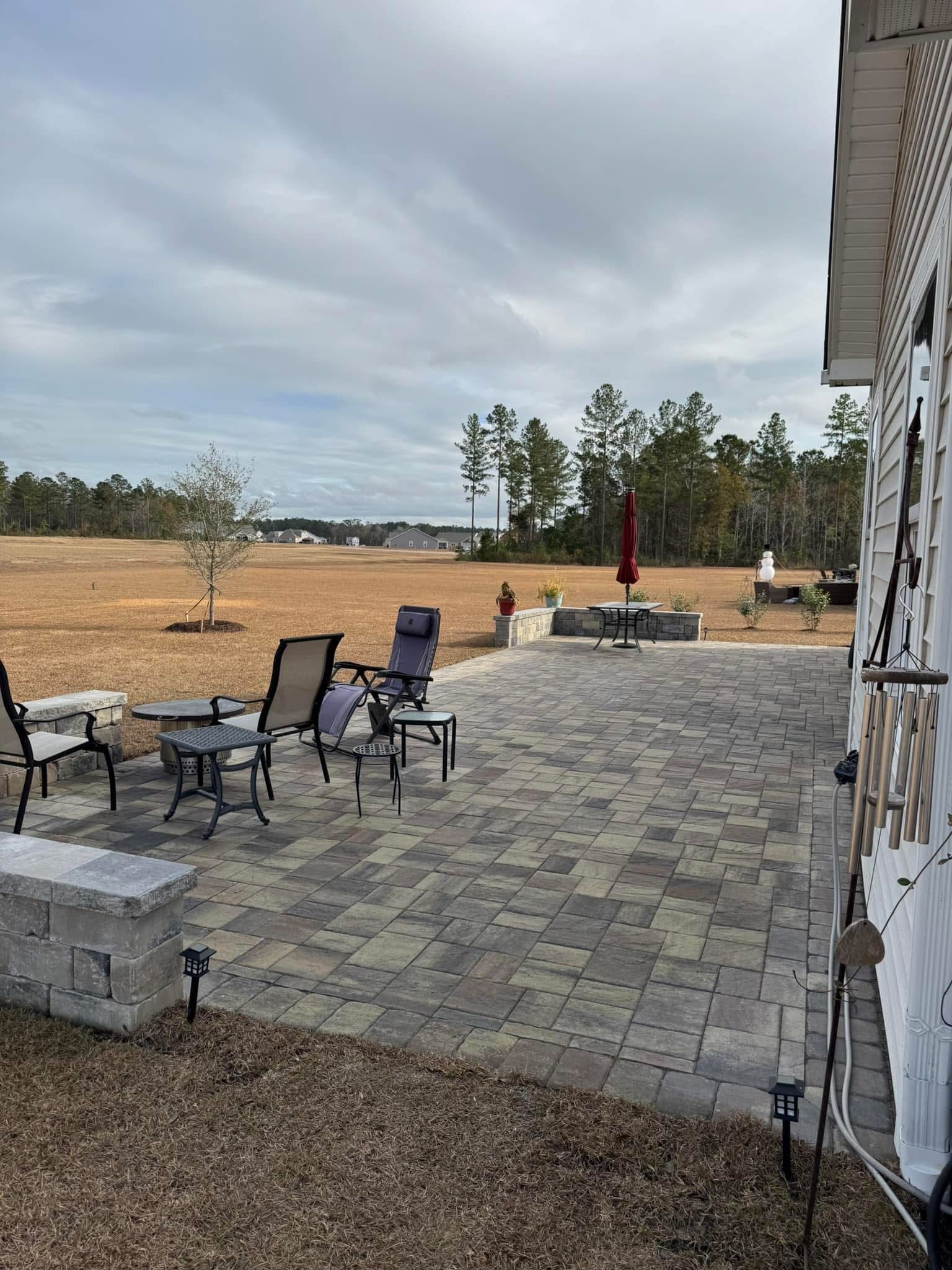 Patio with gray pavers, outdoor seating, and a red umbrella, with a field in the background.