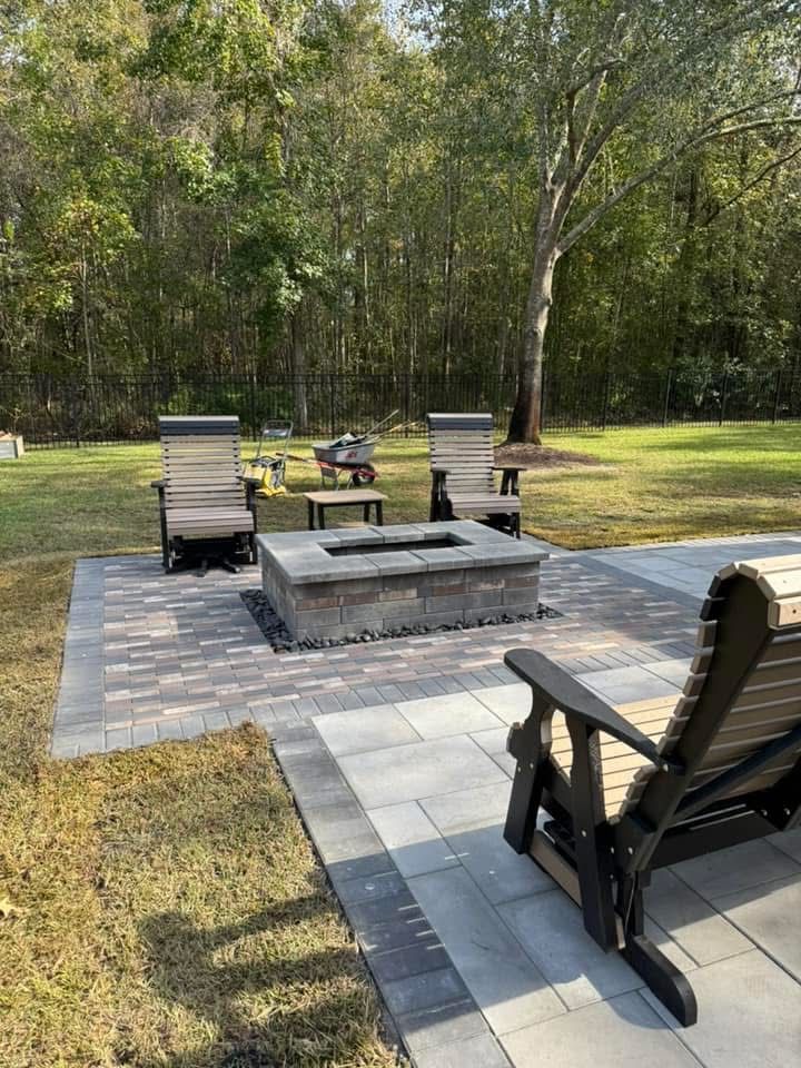 Outdoor patio with fire pit and chairs in a grassy yard, surrounded by trees.