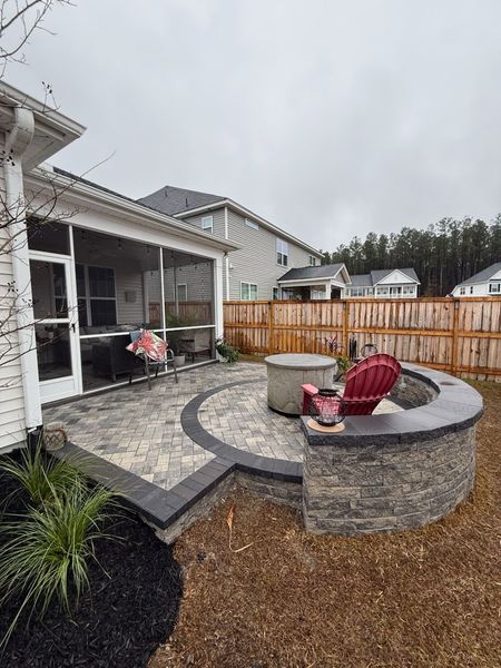 Backyard patio with fire pit, seating, and screened porch against a cloudy sky.
