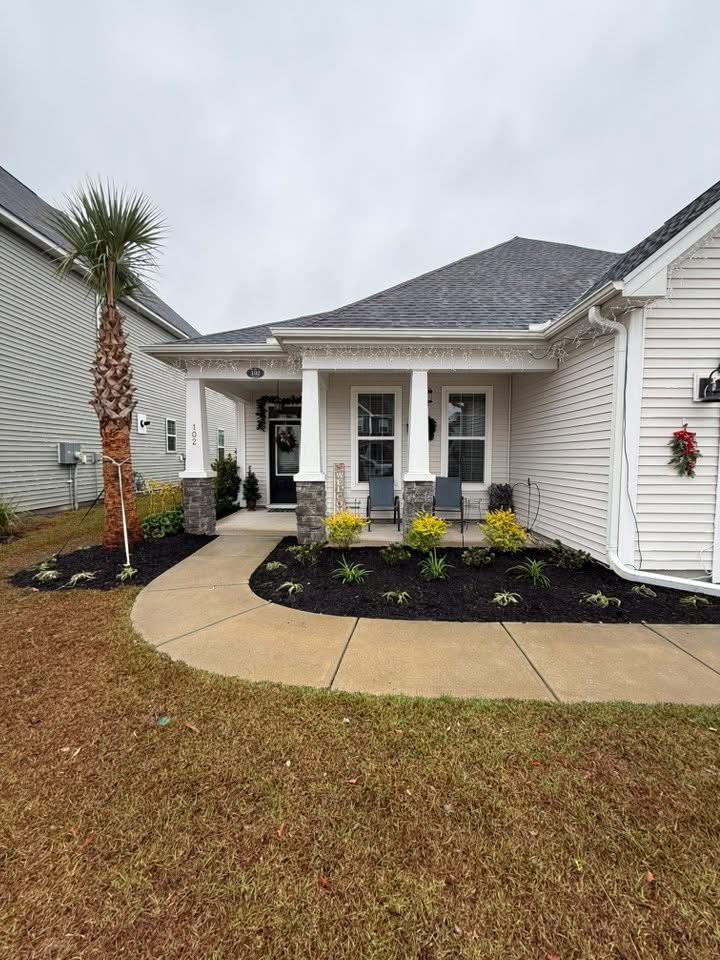 A single-story house with a porch. A walkway leads to the front door, with dark mulch and plants in front.