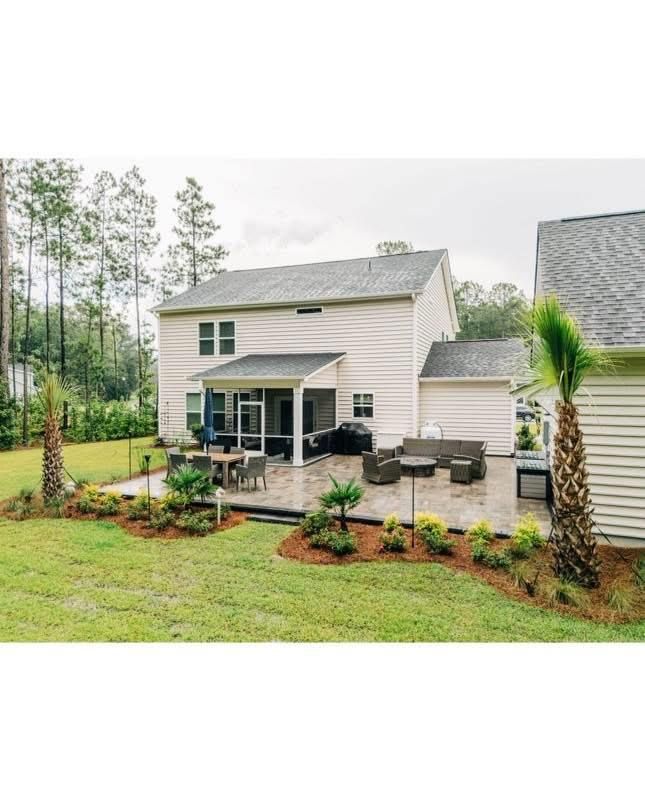 Backyard patio with seating and landscaping, next to a two-story beige house.