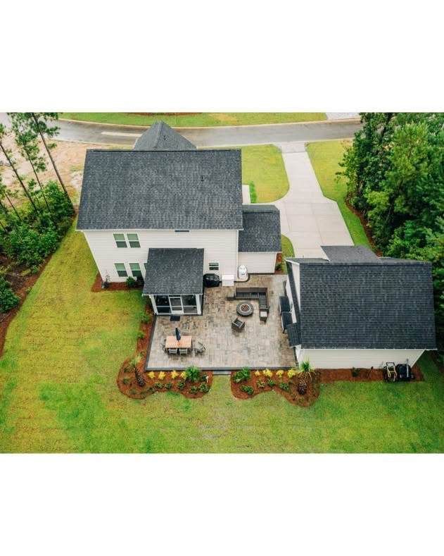 Overhead view of a white house with a gray roof and patio, surrounded by green grass and trees.