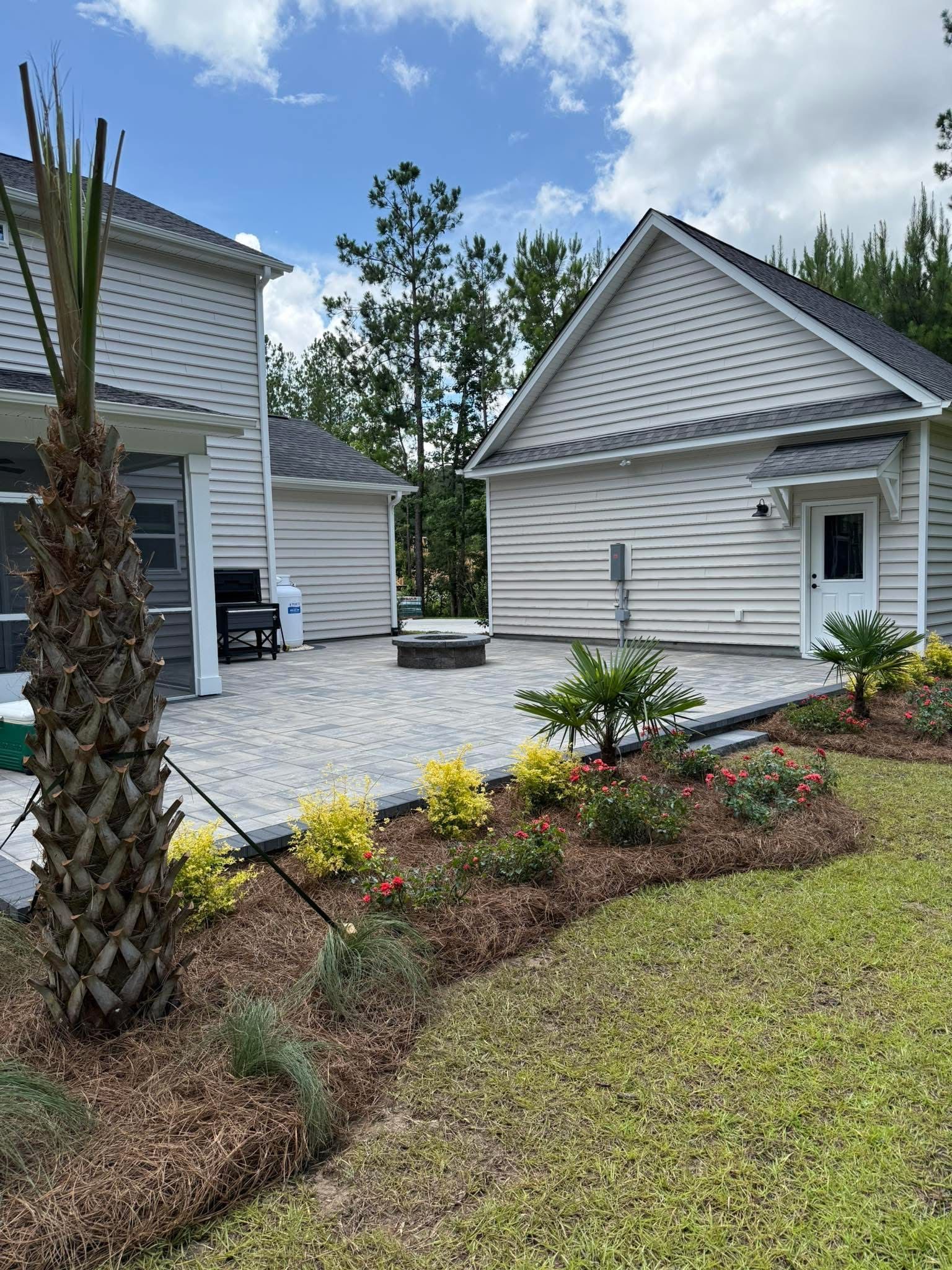 Backyard patio with patterned pavers, garden beds, and two-story house.