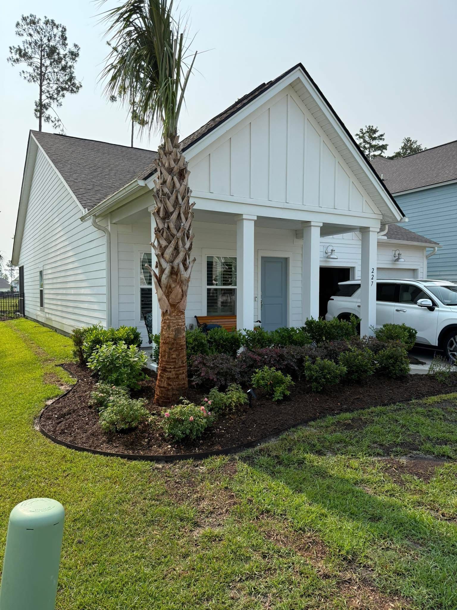 White house with a small porch, palm tree, and a bed of flowers in front.