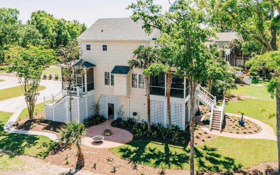 Beige two-story house with screened porches, steps, and landscaping; trees surround the home.