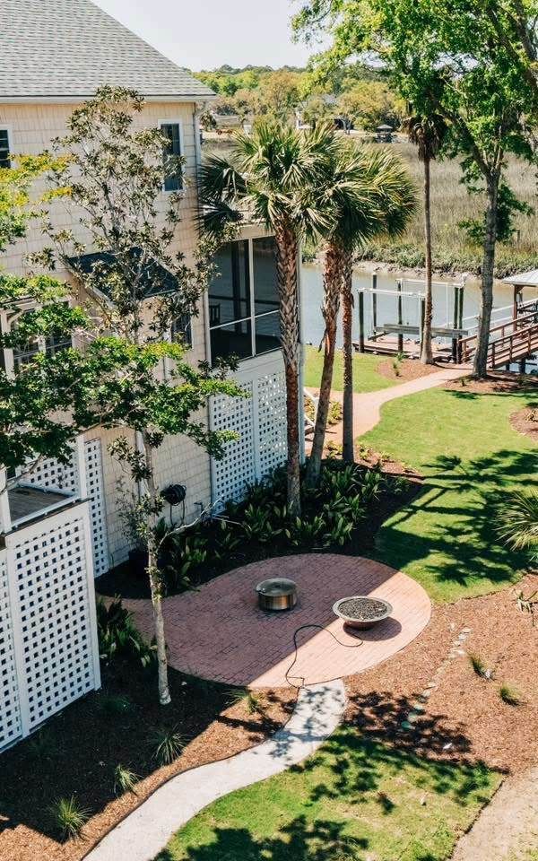 Lush green yard with a paver patio and seating in front of a white building with a screened porch and palm trees.