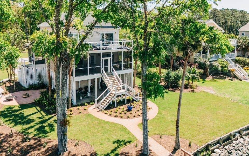Coastal house with screened porch, upper deck, and waterfront view, surrounded by trees and lawn.