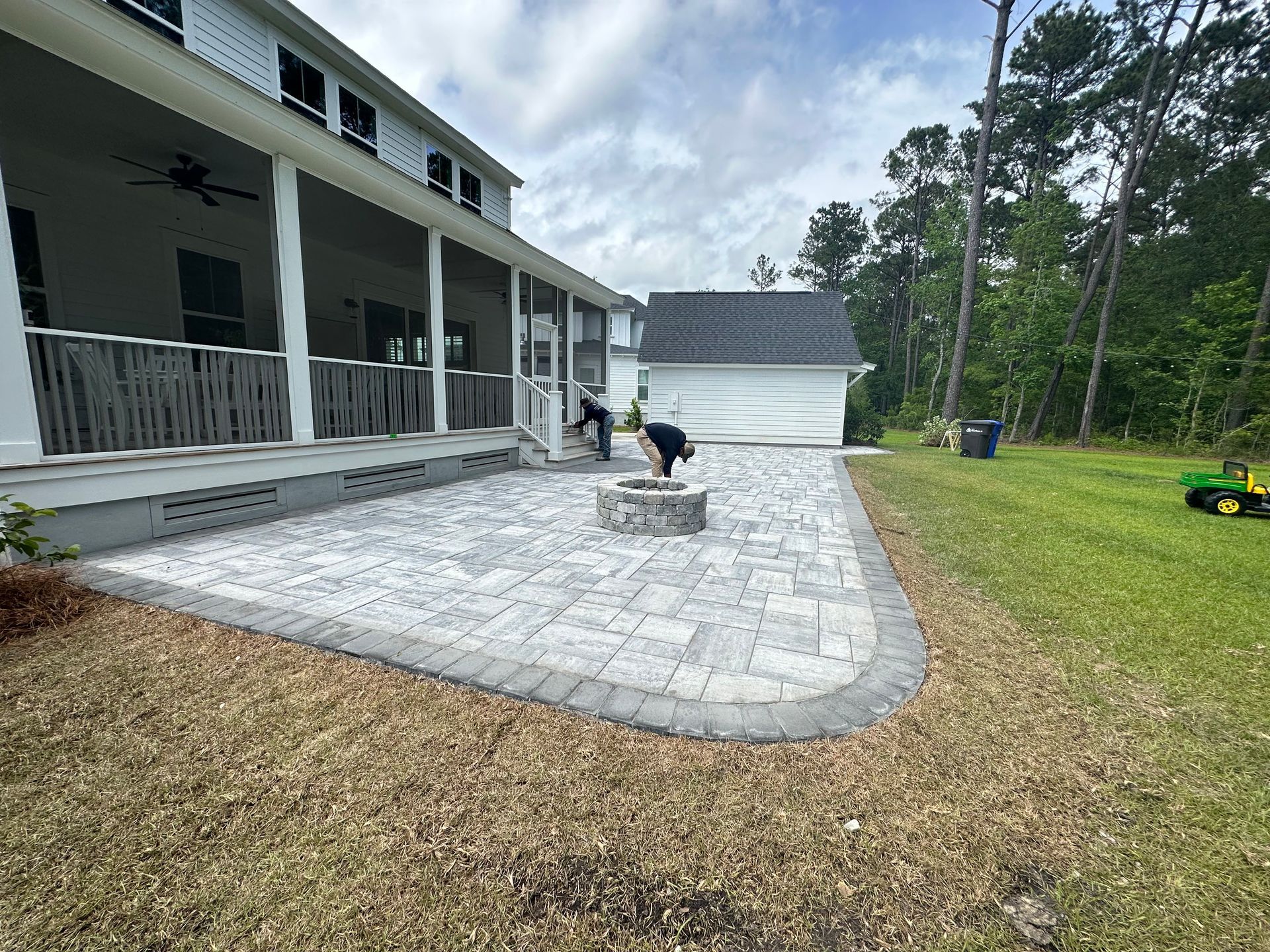 Patio with fire pit in front of a house; two people working.
