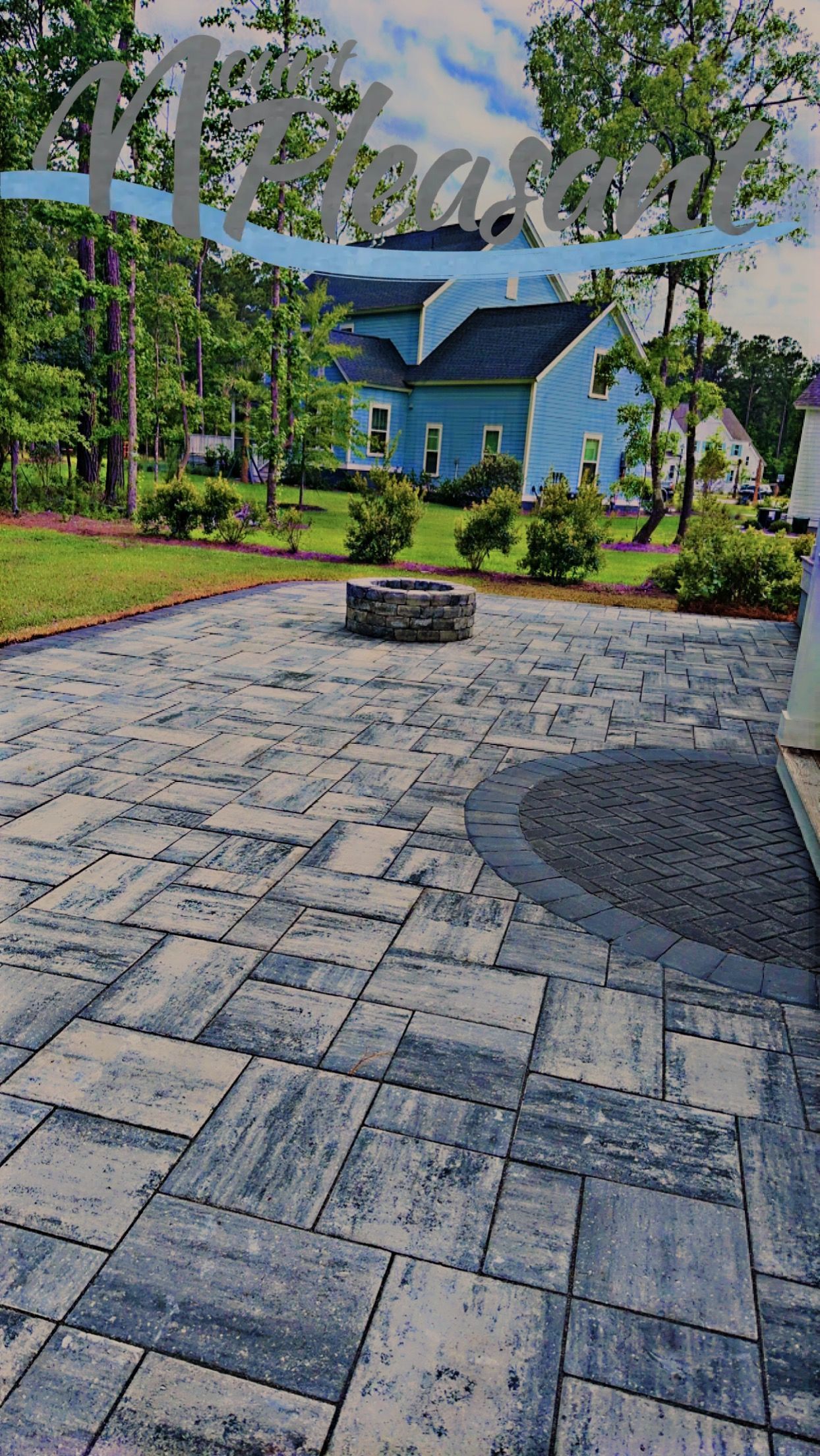 Stone patio with fire pit, blue house in background, trees and landscaping.
